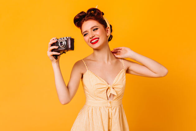 表情快乐的小女孩穿着裙子拍照摄影棚拍摄的优雅的笑脸女子与相机隔离在黄色的空间时尚休闲化妆