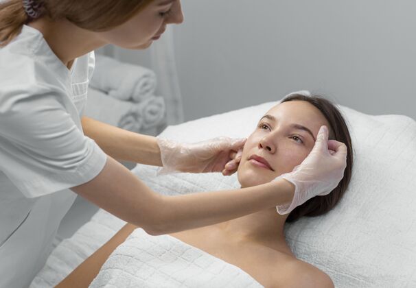 女人美容师与女性客户在沙龙进行面部护理化妆品女人美容治疗