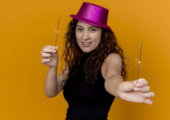 女人一位年轻漂亮的女士 卷发 戴着派对帽 站在橙色的墙上 脸上闪烁着幸福快乐的笑容卷发表演微笑
