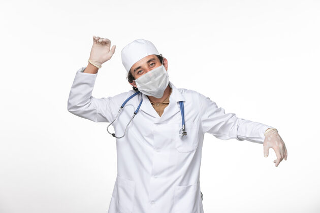 冠状病毒正面图：男医生穿着医疗服 戴着口罩以防感染冠状病毒-在白色墙壁上轻轻舞动飞溅病毒冠状病毒大流行男人面具病毒