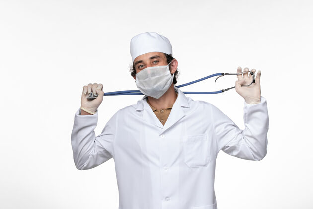病毒正面图：男医生穿着医疗服 戴着口罩 以防柯维德-白墙病毒疾病-健康柯维德-大流行医生正面视图