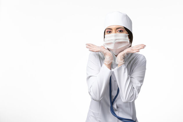 女性前视图：女医生穿着白色医疗服 戴着口罩 因大流行在白墙上摆姿势 健康医学大流行covid-姿势视图冠状病毒