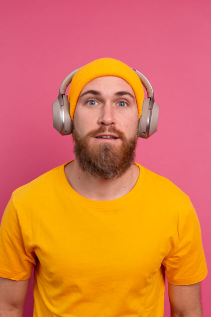 听力帅哥在随意地听着音乐 用耳机隔离在粉色背景上技术男性年轻