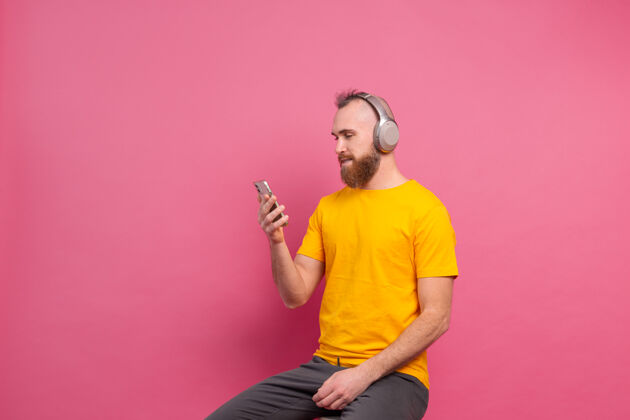 男人帅哥在随意地听着音乐 用耳机隔离在粉色背景上耳机情感音频