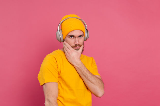 播放列表帅哥在随意地听着音乐 用耳机隔离在粉色背景上情人家伙旋律