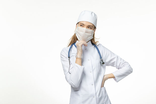 思考正面图女医生穿着医疗服戴着口罩和手套因冠状病毒思考白桌病病毒冠状病毒-大流行性疾病到期听诊器手套