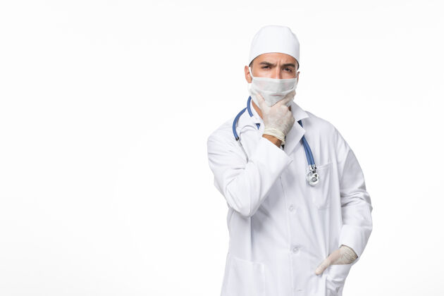 冠状病毒正面图：男医生穿着医疗服 戴着口罩 因为柯维德-思考白墙疾病病毒柯维德-大流行疾病思考大流行男性