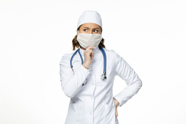 正面正面图身着白色医疗服 戴着口罩的女医生思考着白墙上的潘多米病毒病药套装病毒疾病