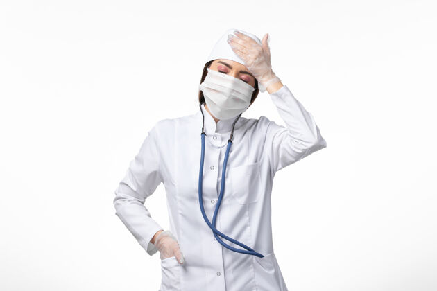 面罩正面图女医生穿着白色无菌医疗服 带口罩 因白墙上有冠状病毒头痛病大流行病毒冠状病毒实验室外套头痛人员
