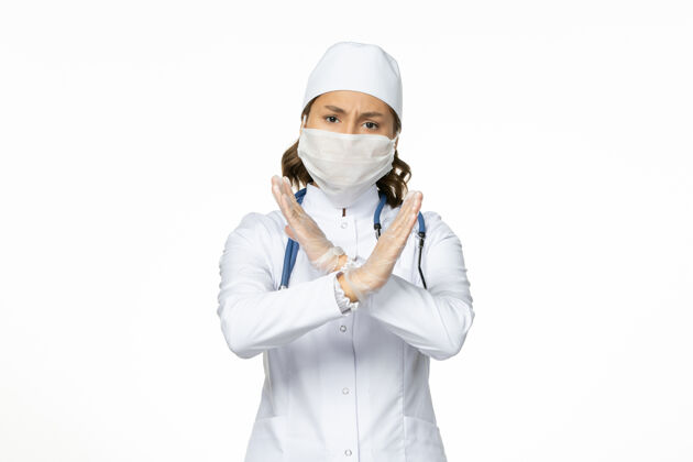 成人正面图女医生穿着白色医疗服 戴着口罩 因白墙上有冠状病毒大流行性疾病隔离冠状病毒面罩医生视图