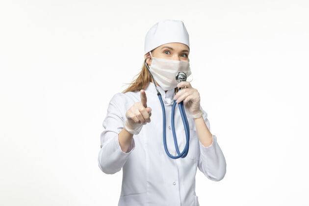 仪器前视图穿着白色医疗服的女医生在白墙上使用听诊器疾病冠状病毒-大流行疾病医院套装医疗器械