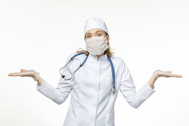 制服正面图女医生穿着医疗服戴口罩因白墙上冠状病毒病大流行疾病冠状病毒预防专业医疗