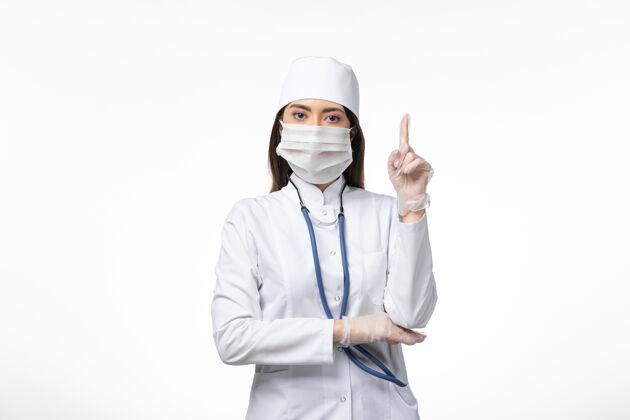 手指正面图：女医生穿着白色无菌医疗服 带着口罩 因为柯维德-抬起手指白墙病柯维德-大流行病毒病大流行人专业