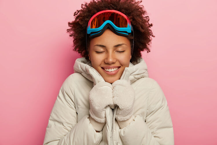 滑雪板可爱的深色皮肤的女滑雪运动员穿着冬衣 戴着手套 愉快地微笑 表达快乐的情绪 享受娱乐时光特写粉色高兴