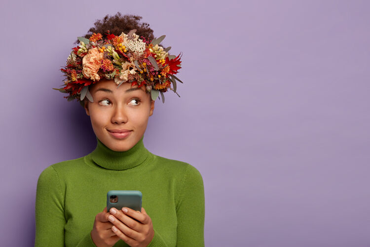 跳投可爱体贴的秋天女士戴着自然的花环 用手机上网购物 专注在一边 隔着紫色的墙与世隔绝非洲立场紫色