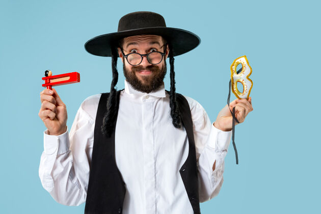面具一个年轻的东正教犹太男子与木制棘轮在普瑞姆节画像犹太教堂节日信仰