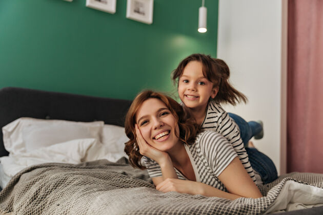 房间小女人和她的妈妈躺在床上 笑着看着镜头微笑可爱玩