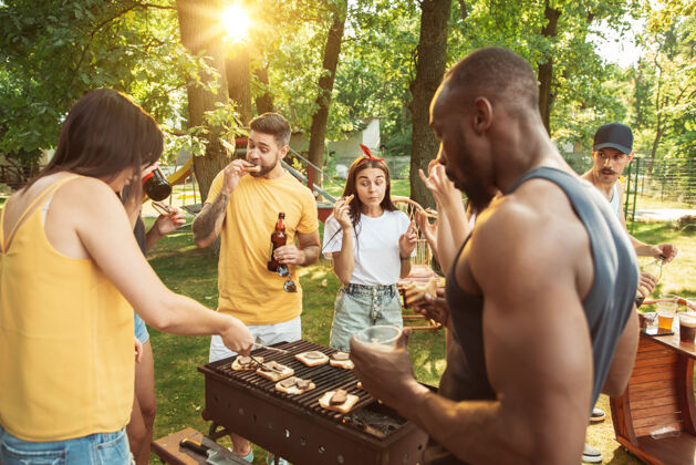 花园一群快乐的朋友在阳光明媚的日子里喝着啤酒 一起烧烤一起在户外的林间空地或后院休息烧烤庆典酒精