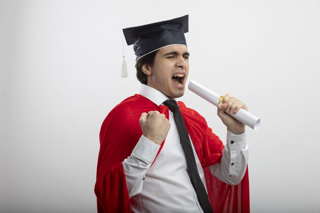 举行快乐的年轻超级英雄戴着领带 戴着毕业帽 拿着毕业证书 唱着“是”的手势家伙穿是的