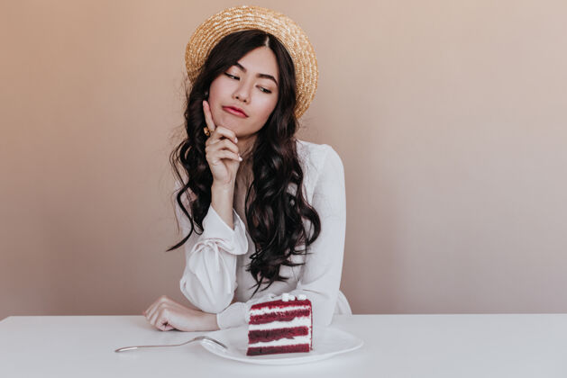 沉思沉思的亚洲模特看着蛋糕犹豫不决的日本女人拿着甜点摆姿势发型摄影棚拍摄件
