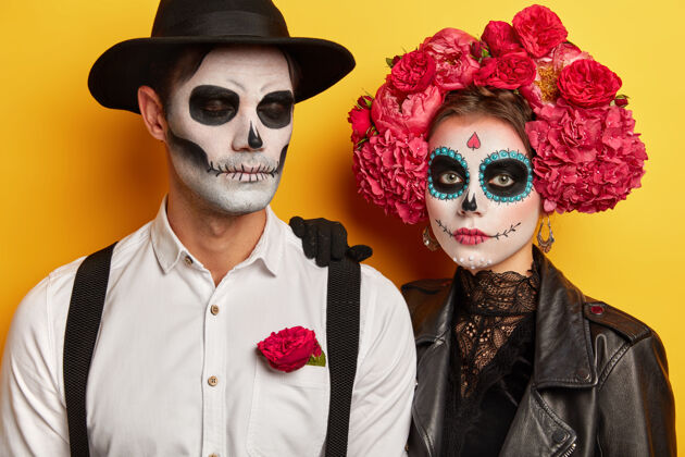皮革摄影棚拍摄的严肃情侣穿着生动的妆容 庆祝墨西哥传统节日 戴花环 来化装舞会 隔离在黄色背景下死亡日概念传统衬衫严重