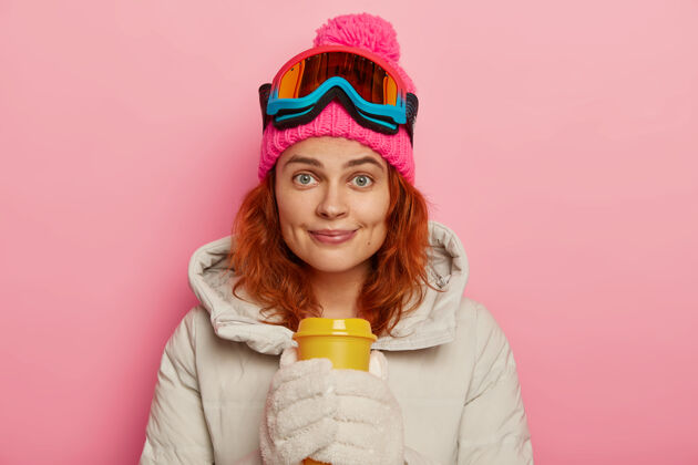 红发美丽的姜女少年喜欢极限运动 滑雪后喝咖啡 愉快地看着镜头 戴着滑雪镜女孩帽子红发