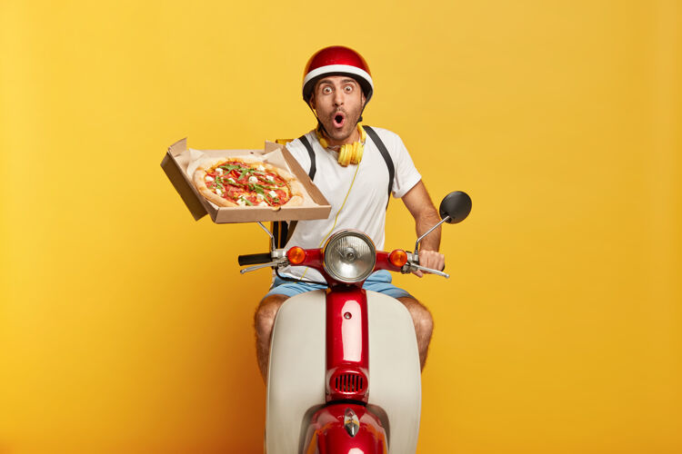 美味惊呆了的英俊男司机骑着摩托车 戴着红色头盔送比萨饼休闲披萨路线