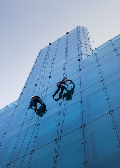 人垂直低角度拍摄两个人在白天攀爬一座高玻璃建筑街道方式顶部