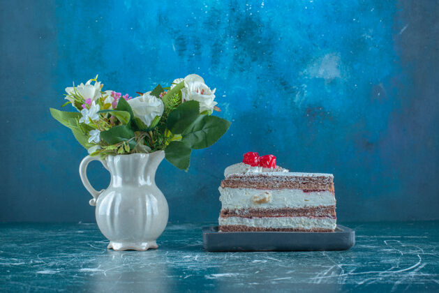 甜点蓝色背景上的一小片蛋糕旁边放着一束鲜花高质量的照片糖糕点包