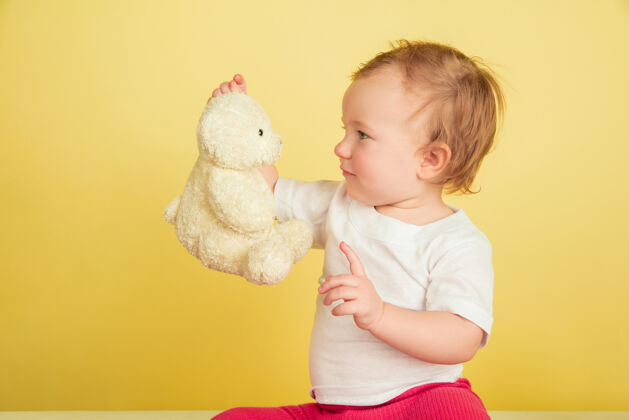 游戏白人小女孩 黄色工作室背景上孤立的孩子们可爱可爱的孩子的肖像 和泰迪熊玩耍的宝宝情感游戏黄色