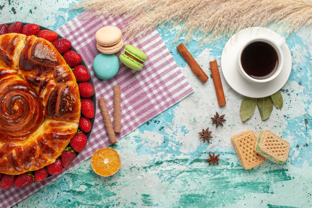 曲奇俯瞰草莓派 配华夫饼 法式马卡龙和蓝色表面的一杯茶饮料饼干早餐