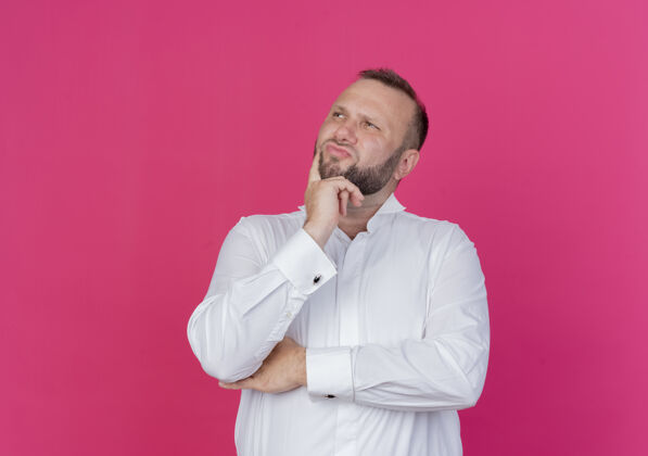站一个留着胡子的穿白衬衫的男人站在粉红色的墙上 困惑地看着一边靠边拼图胡子