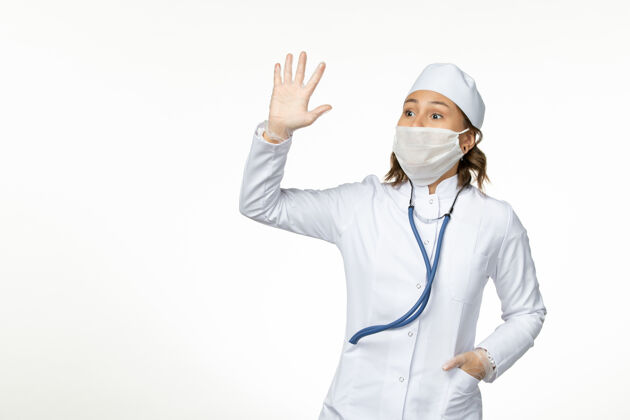 到期正面图年轻女医生戴防护无菌口罩因冠状病毒在白色表面挥舞病毒冠状病毒灭菌