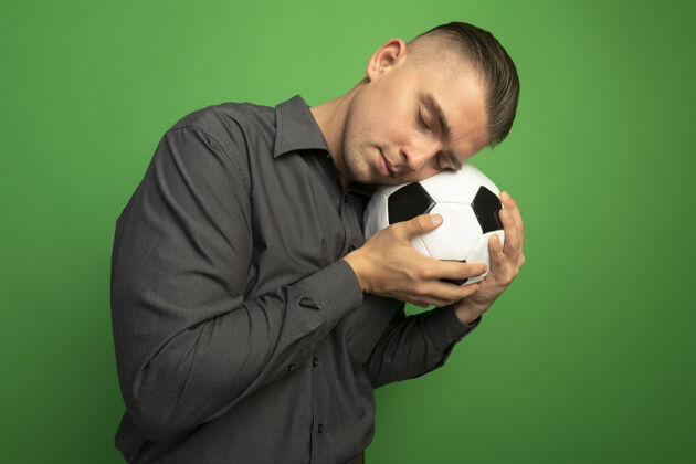 封闭穿着灰色衬衫的年轻帅哥 举着足球 闭着眼睛把头靠在球上衬衫持有男子
