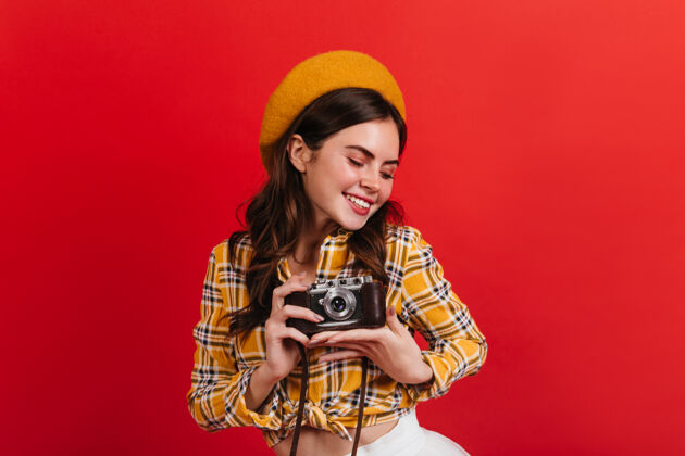 服装活跃的女士在红墙上微笑可爱黑发女士用复古相机拍照乐趣法国女孩