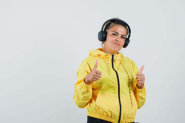 民族戴着耳机欣赏音乐的女人 在运动服前视图中展示拇指微笑享受西装