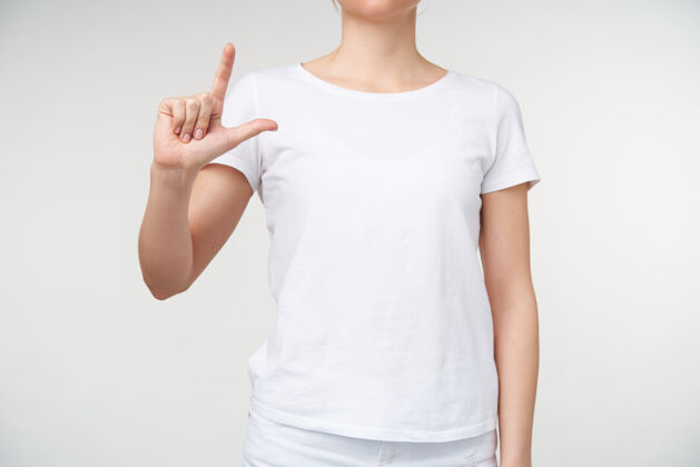 符号室内拍摄的年轻女性举起她的手 同时形成与手指字母l 学习聋哑字母 而被隔离在白色背景符号女性皮肤白皙