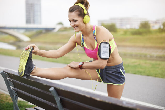 肌肉年轻女子户外运动长凳是一个伟大的帮助 而伸展跑道短裤人体
