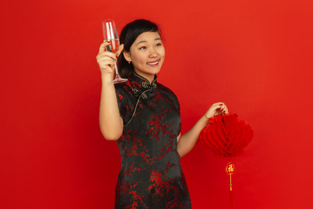 亚洲喝着香槟 捧着灯笼中国新年快乐红色背景上的亚洲少女肖像身着传统服装的女模特看起来很快乐复制空间旗袍庆祝手