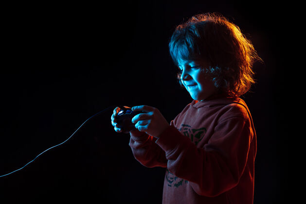 面部参加玩电子游戏在霓虹灯下的黑暗工作室背景上的白人男孩肖像美丽的卷曲模型情绪屏幕显示
