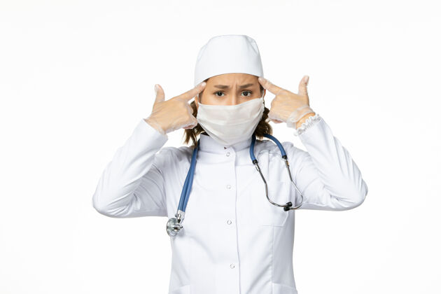 大流行正面图年轻女医生戴着无菌口罩和手套 由于冠状病毒在浅白的表面制服灭菌正面