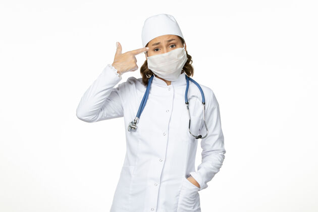 西装前视图年轻的女医生穿着白色的医疗服 戴着口罩 因为白色的地板上有冠状病毒口罩专业疾病