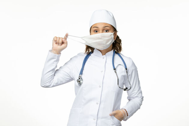 专业正面图年轻的女医生 戴着冠状病毒防护面具 在浅白的表面微笑医生正面大流行