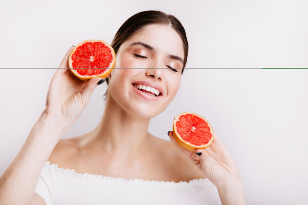 不化妆心情愉快的女孩可爱地笑在白色的墙上 手里拿着美味可口的柑橘类水果清晰头发新鲜