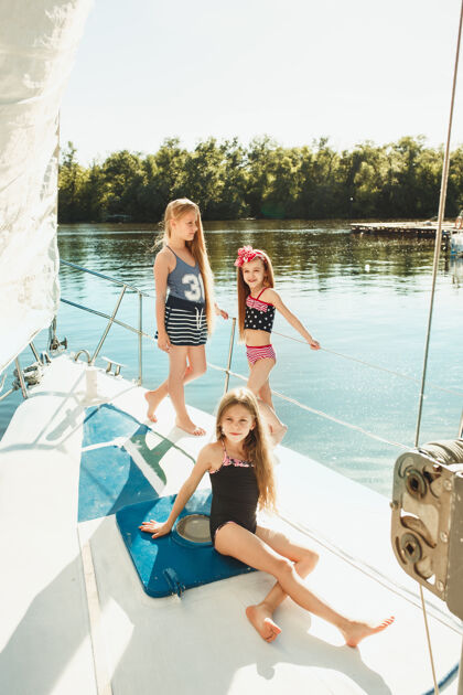 衣服孩子们在游艇上喝着橙汁青少年或少女们在蓝天下户外五颜六色的衣服孩子们的时尚 阳光明媚的夏天 河流和假日的概念青少年船户外