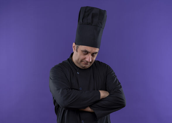 怀疑男厨师身穿黑色制服 头戴厨师帽 面带怀疑的表情 双手交叉放在胸前 站在紫色背景下 看着镜头皱眉表情交叉