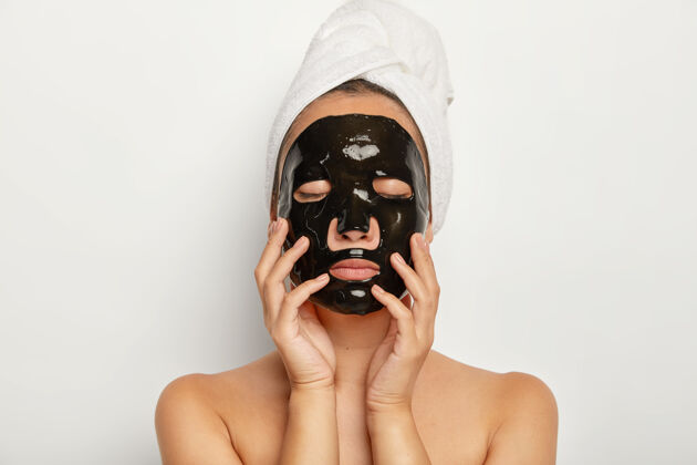 人类特重的年轻女子拍下的黑色面罩 闭上眼睛 轻轻触摸脸部 头围裹着毛巾模特治疗肖像