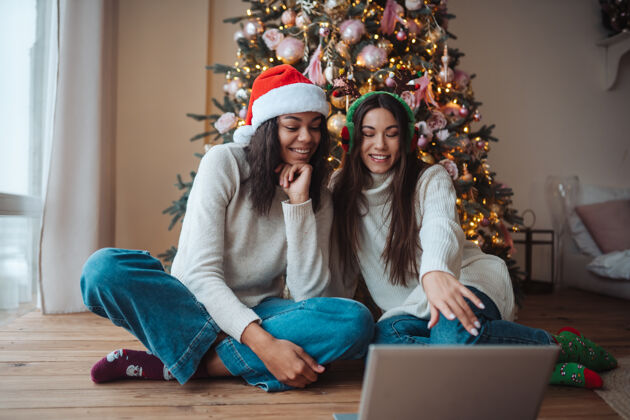 礼物两个女孩在家里庆祝圣诞节时微笑着用笔记本电脑和网友聊天在线驯鹿多民族