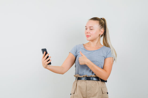 人穿着t恤 裤子的年轻女性在视频聊天中竖起大拇指 看上去很快乐 正面视图黑发年轻时尚