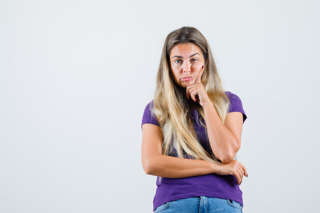 女人身着紫罗兰色t恤 牛仔裤的年轻女士站在思考的姿势中 神情犹豫不决 俯视前方看黑发女性